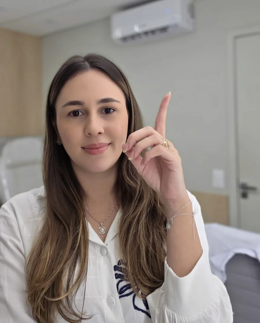 Emanuelle Abud em uma fotografia no consultório, com a mão levantada